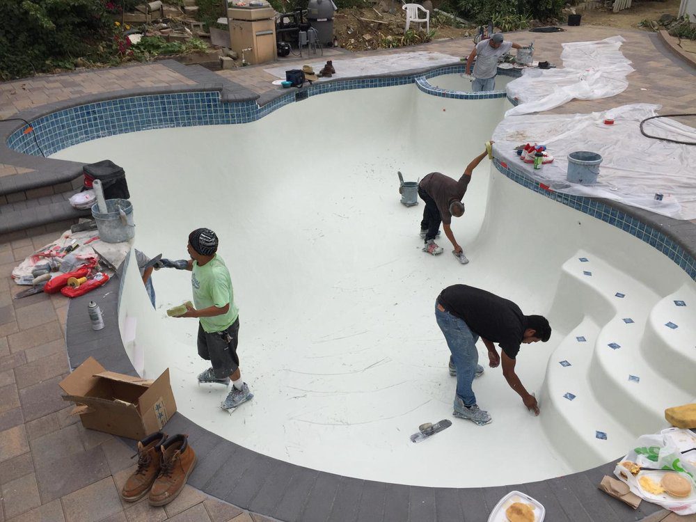 Three men work inside an empty swimming pool to seal and paint the basin