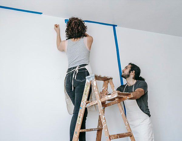 Two people remove painter’s tape from a freshly painted white wall